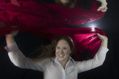 Smiling young woman holding red scarf in underwater