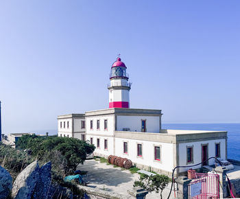 Lighthouse by sea against clear blue sky
