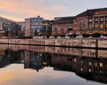 Bridge over river by buildings against sky during sunset