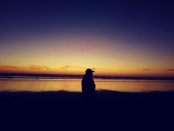 Silhouette woman standing at beach against sky during sunset