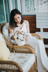 Woman holding flower while sitting on chair