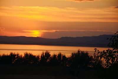 Scenic view of lake and mountains against cloudy orange sky during sunset