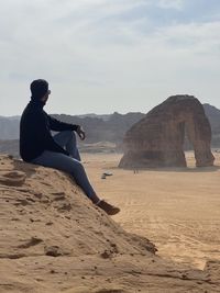 Man sitting on cliff against sky