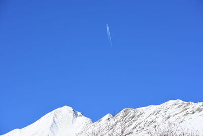 Low angle view of snowcapped mountains against blue sky