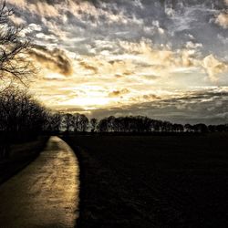 Road amidst field against sky during sunset