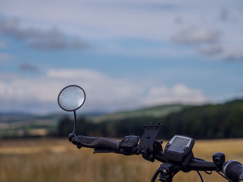 Close-up of bicycle on field against cloudy sky