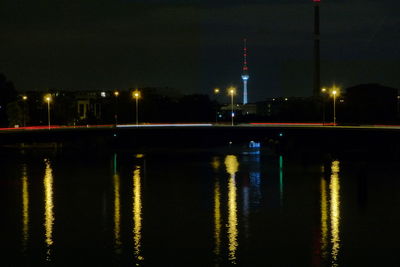 Illuminated buildings by river against sky at night