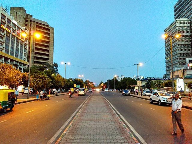 building exterior, transportation, city, architecture, built structure, the way forward, street, clear sky, road, street light, car, road marking, diminishing perspective, city street, city life, illuminated, land vehicle, mode of transport, vanishing point, sky