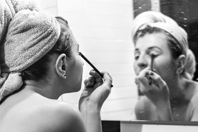 Young woman applying mascara in front of mirror