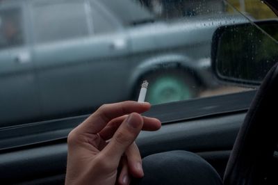 Cropped image of person holding cigarette in car during monsoon