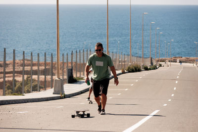 A man playing figure skating on a rural road in the sun on a bright day, play surf skate near coast