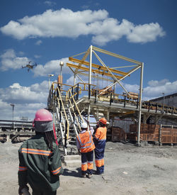Rear view of people working at construction site against sky