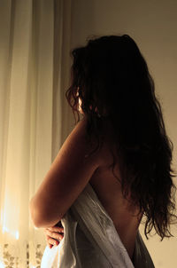 Side view of naked woman covered with blanket by wall