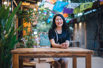 Portrait of a smiling young woman sitting on table at restaurant