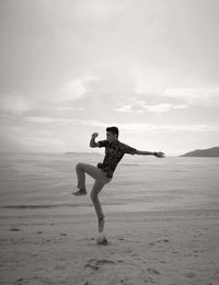 Full length of man jumping at beach against sky