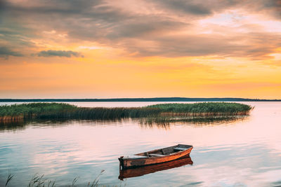 Boat moored in lake against sky during sunset