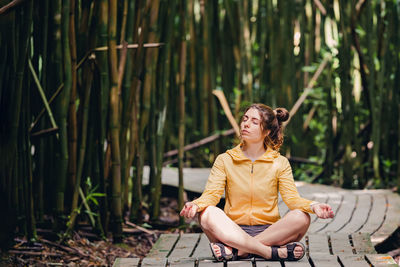 Young woman sitting in meditation pose, relaxing among the bamboo tress.