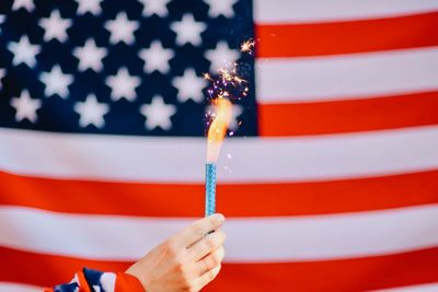 Cropped hand holding lit firework against american flag