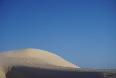 Low angle view of sand dunes against clear blue sky