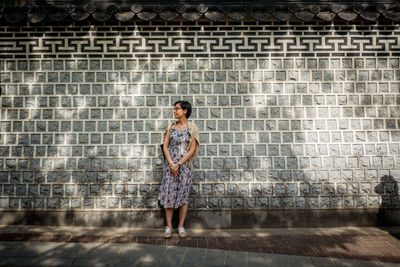 Full length portrait of woman standing against wall