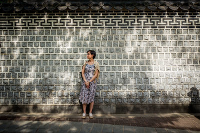 Full length of woman standing against wall on footpath