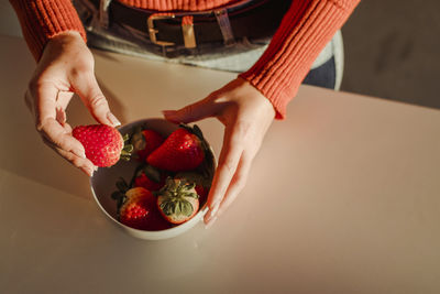 Woman holding fresh strawberries at dining table at home