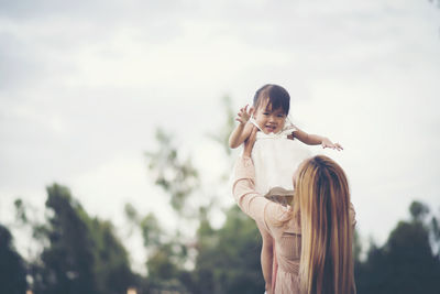 Mother carrying daughter while standing against sky