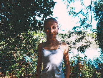 Portrait of young woman standing against trees