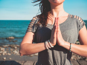 Midsection of young woman doing yoga on pier at beach