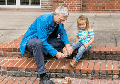 Full length of senior man helping granddaughter in wearing shoe outdoors