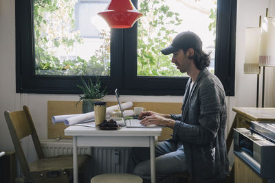Side view of male architect using laptop at desk in home office