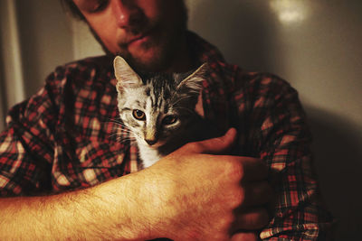 Midsection of man holding cat sitting at home