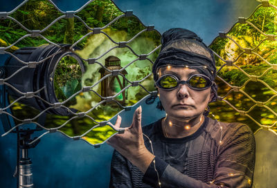 Digital composite image of woman with forest seen through chainlink fence