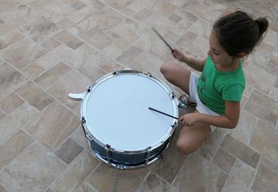 High angle view of girl playing drum while crouching on floor