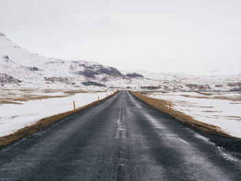 Road leading towards snowcapped mountain against sky