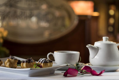 Close-up of profiteroles in tray by cup and teapot on table