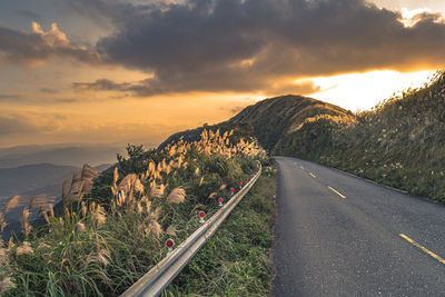 Road by mountains against sky during sunset