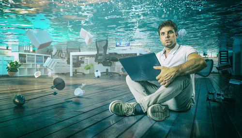 Portrait of businessman using laptop while office sunk in water