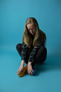 Portrait of young woman sitting on blue background