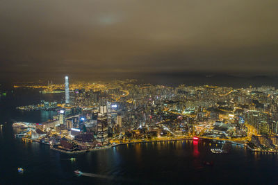 High angle view of illuminated buildings by sea against sky at night