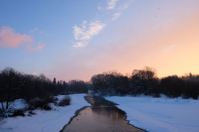 Snow covered landscape against sky during sunset