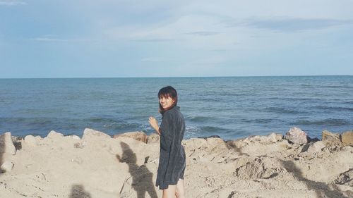 Portrait of woman standing on rock formation by sea against sky