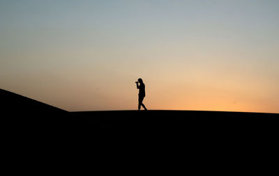 Silhouette person standing on field against sky during sunset