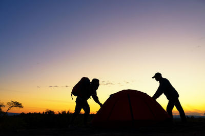 Side view of hikers standing by tent on field against sky