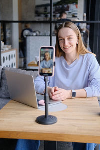 Young beautiful woman blogger making a video for her blog using phone camera in a cafe.