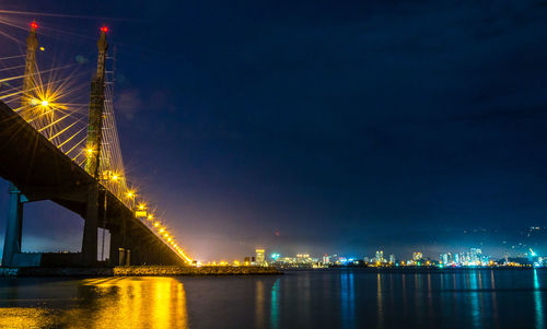 Illuminated city by river against sky at night