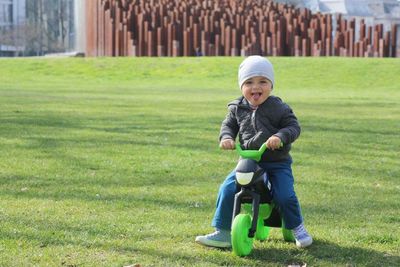 Portrait of baby boy riding tricycle on grassy field