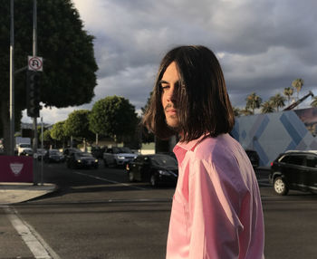 Man with long hair standing on road against sky