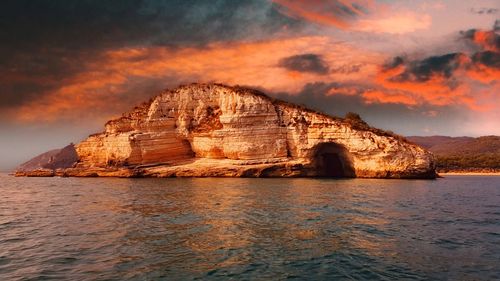 Rock formation in sea against sky during sunset