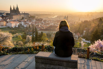 Rear view of woman relaxing outside in city park and enjoying view of prague, beautiful sunrise